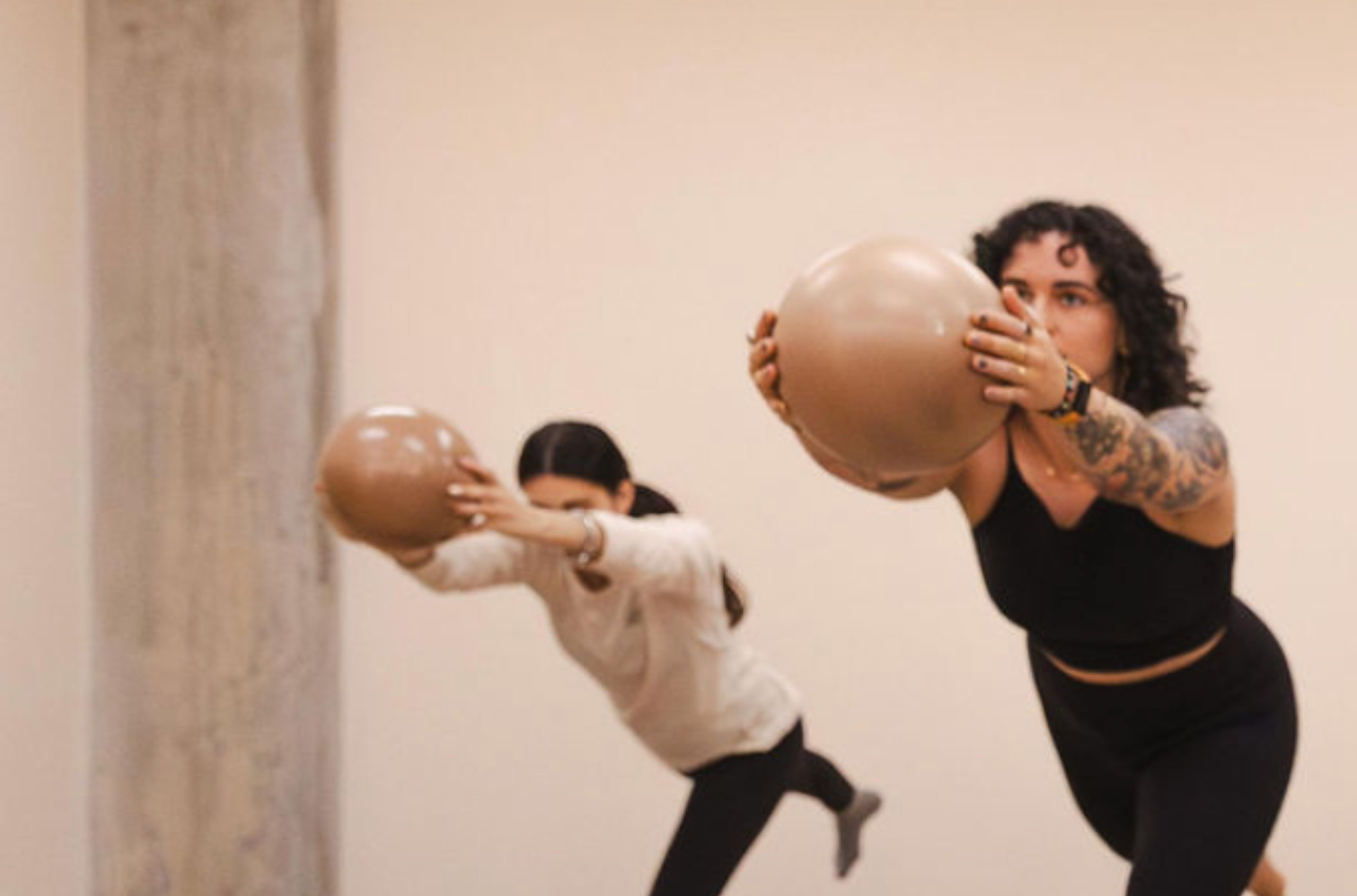 Deux femmes dans une position de Pilates avec chacune un ballon dans les mains durant un cours de Pilates sur la Rive-Sud.
